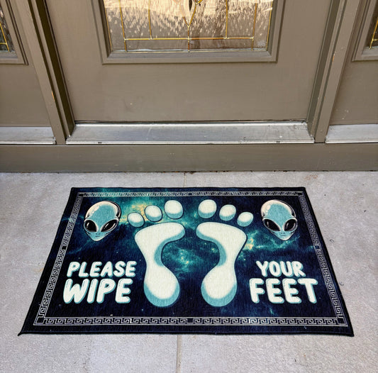 Doormat with alien design and text 'Please Wipe Your Feet' at a front door